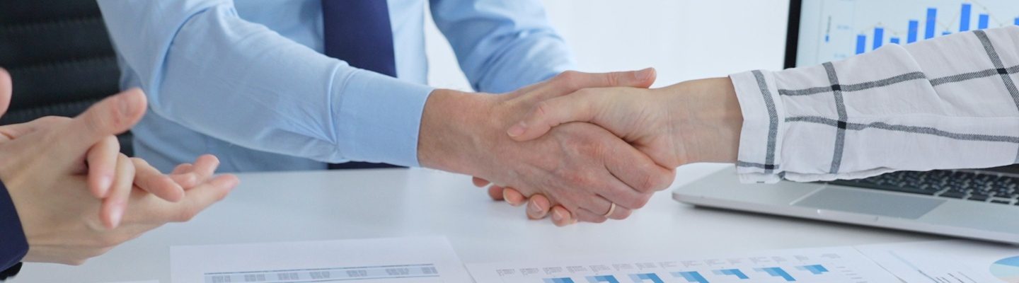 Business people are shaking hands and applauding, finalizing a deal while reviewing financial documents, graphs, and charts on a desk in a modern office environment